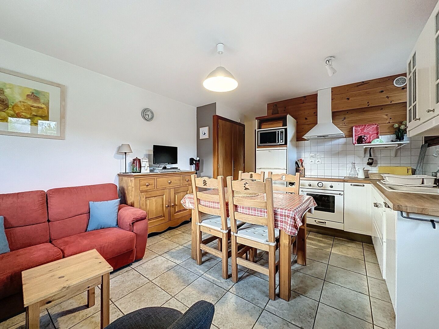 A compact living space with a kitchenette, a dining area with wooden chairs, a red sofa, and a small table.