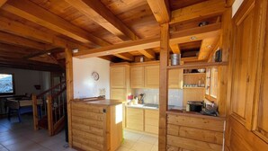 A wooden cabin interior with a kitchen area, wooden cabinets, and a dining table. - Chalet face aux étoiles (Molines-en-Queyras)