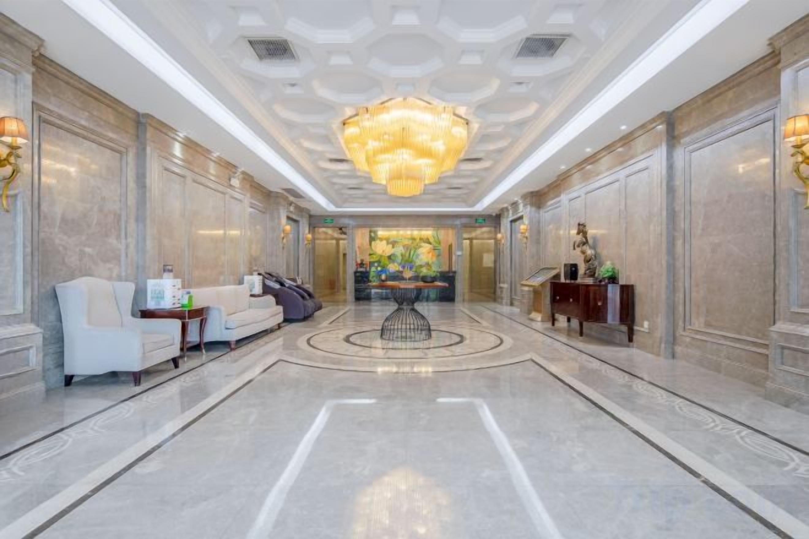 A hotel lobby with a central seating area, a chandelier, and a reception desk.