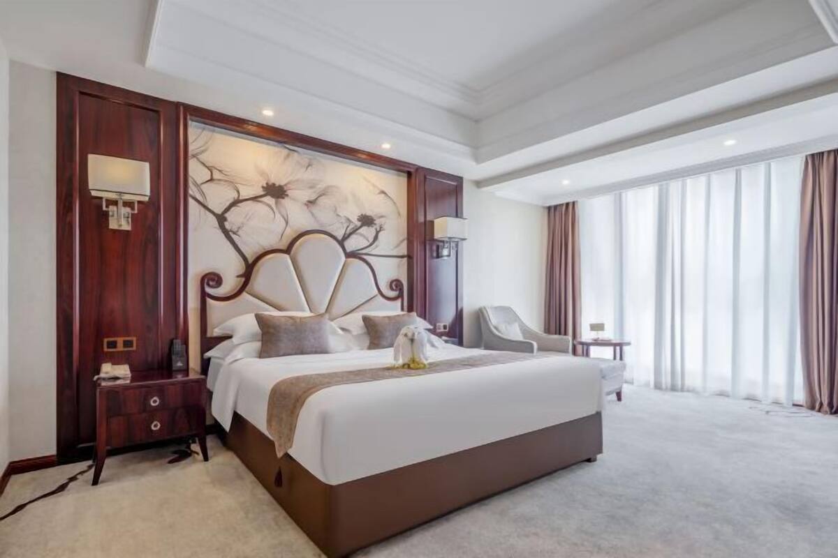 A large bed with a headboard, a bedside table, a lamp, and a chair in a hotel room.