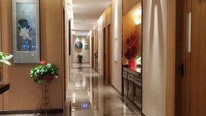 A hotel corridor with a polished floor, wooden walls, and a reception area with a plant and a vase. - Kameidun Hotel (Changsha University of Science and Technology Yuntang Campus) (Changsha)