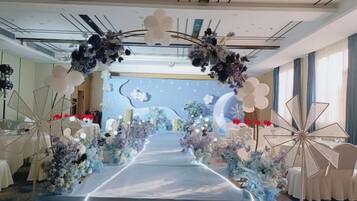 Salão de festas com uma longa mesa, decoração floral e um palco.
