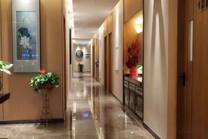 A hotel corridor with a polished floor, potted plants, and a reception area with a counter and seating. - Kameidun Hotel (Changsha University of Science and Technology Yuntang Campus) (Changsha)