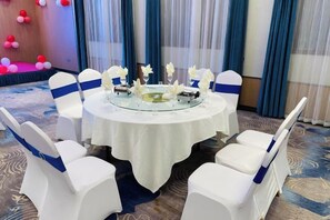 A round table with a glass centerpiece surrounded by white chairs with blue sashes, set on a carpeted floor. - Kameidun Hotel (Changsha University of Science and Technology Yuntang Campus) (Changsha)