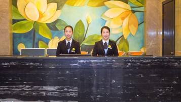 Duas pessoas sentadas em um balcão de atendimento, com um mural floral ao fundo.