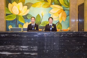 Two individuals seated at a reception desk with a floral mural in the background. - Kameidun Hotel (Changsha University of Science and Technology Yuntang Campus) (Changsha)