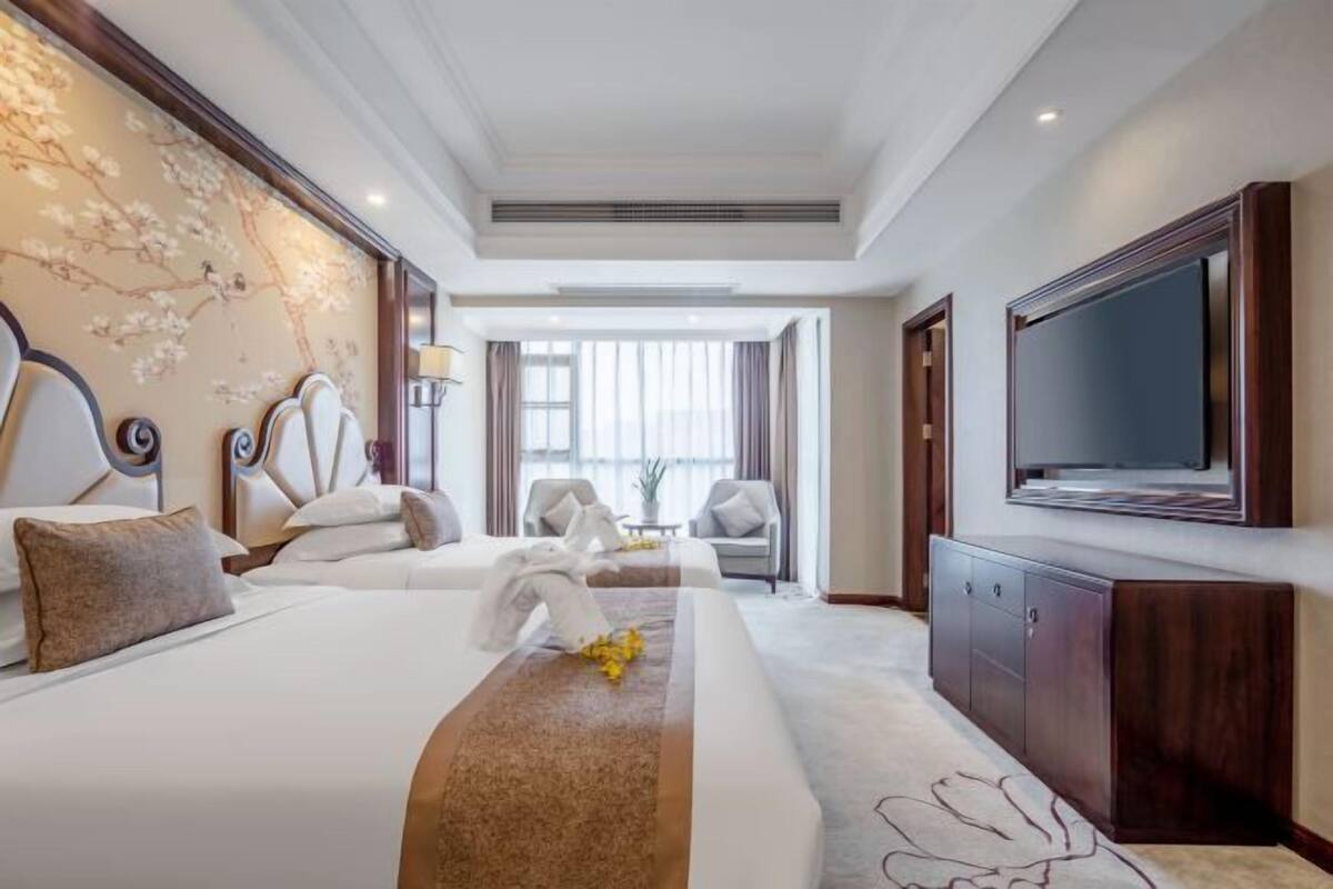 A hotel room with two beds, a television, a desk, and a large window.