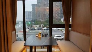 A room with a view of a busy street and tall buildings. There is a table with a lamp and a small plant on it. - Kameidun Hotel (Changsha University of Science and Technology Yuntang Campus) (Changsha)