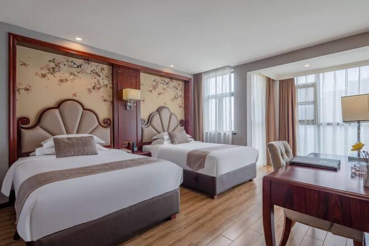 A hotel room with two beds, a desk, and a large window.