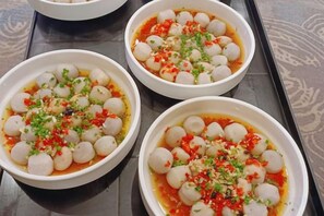 Three bowls of a dish with round items and red sauce, garnished with green herbs, on a tray. - Kameidun Hotel (Changsha University of Science and Technology Yuntang Campus) (Changsha)