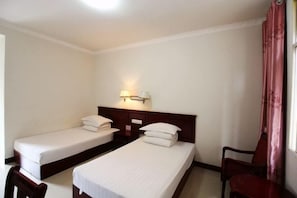 A hotel room with two single beds, a nightstand with a lamp, a chair, and a window with curtains. - Jinghong HuaJing Hotel (Jinghong)