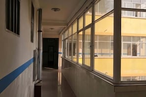 A corridor with a windowed wall, a door at the end, and a blue stripe on the wall. - Jinghong HuaJing Hotel (Jinghong)