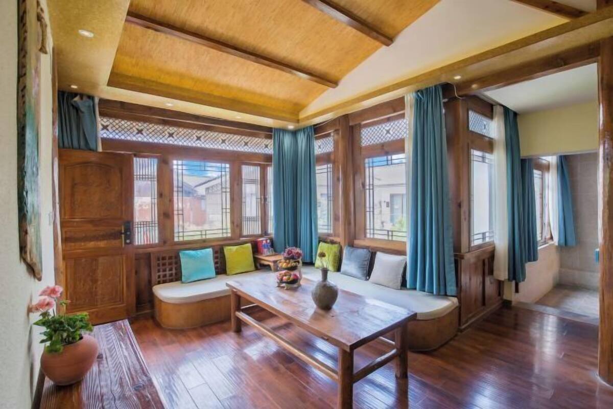 A traditional-style room with wooden floors, a low ceiling, and large windows with blue curtains.