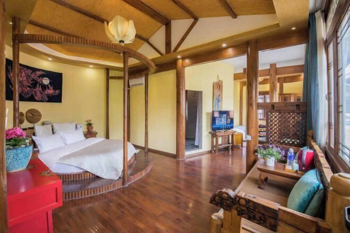 A room with a bed, a wooden bench, a TV, and a large window.