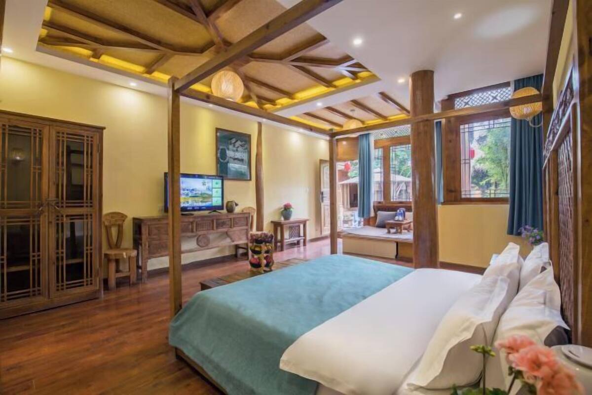 A room with a bed, wooden furniture, a television, and a view of the outdoors.