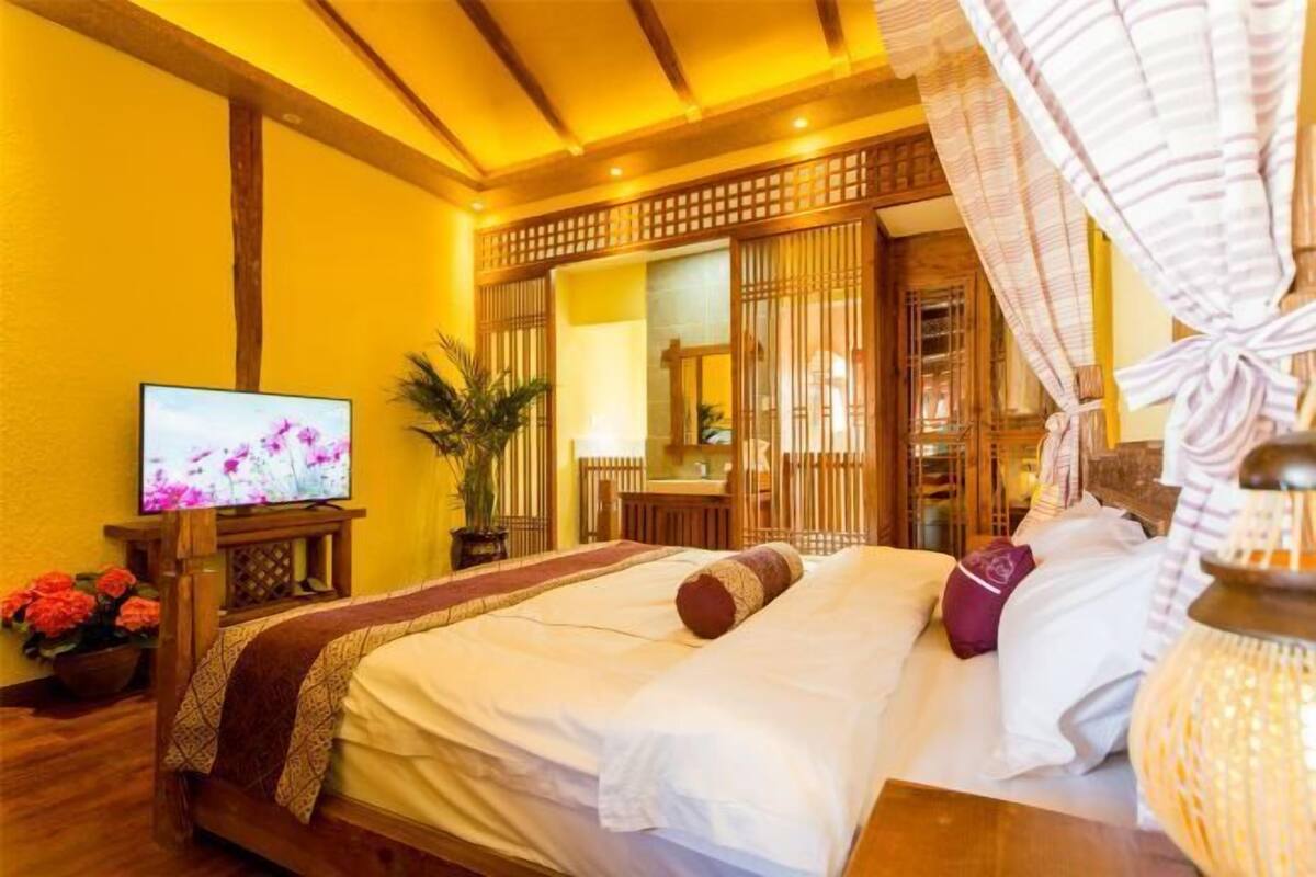 A hotel room with a bed, a television, a potted plant, and a decorative lamp.
