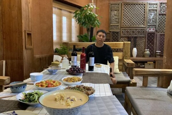 A dining area with a table set for a meal, surrounded by wooden furniture and decorative panels. - Yunmengze Hostel (Lijiang)