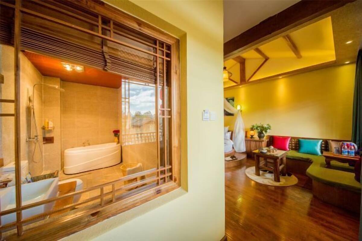 A room with a bathtub, a wooden-framed window, a sofa, and a small table.