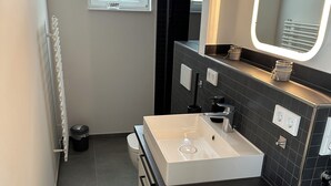 Un bagno compatto con un lavandino bianco, uno specchio, una piccola finestra, un termosifone e una lavatrice.