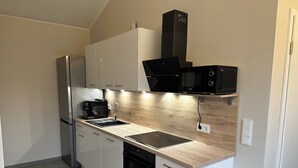Una cucina moderna con mobili bianchi, un frigorifero in acciaio inossidabile, forno integrato, microonde e macchina da caffè.