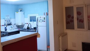 A kitchen with a red countertop, white cabinets, and a refrigerator. There is a window with a flower design on the wall. - Ushuaia hostal  (Ushuaia)