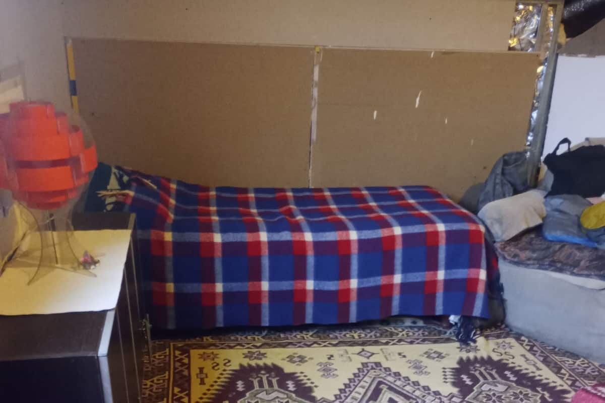 Une pièce avec un lit, une petite table et une chaise. Un tapis à motifs recouvre le sol.