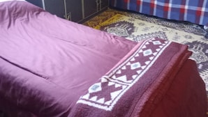 A room with a bed covered in a purple blanket, a blue and red plaid blanket on a chair, and a patterned rug on the floor. - Ushuaia hostal  (Ushuaia)