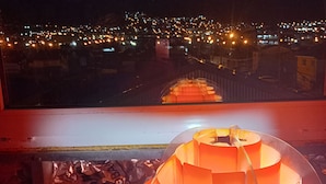 A room with a view of a cityscape at night, a decorative orange lamp, and a patterned tablecloth. - Ushuaia hostal  (Ushuaia)