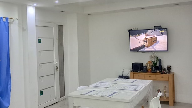 A dining area with a table, chairs, a television mounted on the wall, and a wooden cabinet with decorative items. - Ushuaia hostal  (Ushuaia)