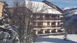 Ein mehrstöckiges Gebäude mit Balkonen, umgeben von schneebedeckten Bäumen und Bergen.