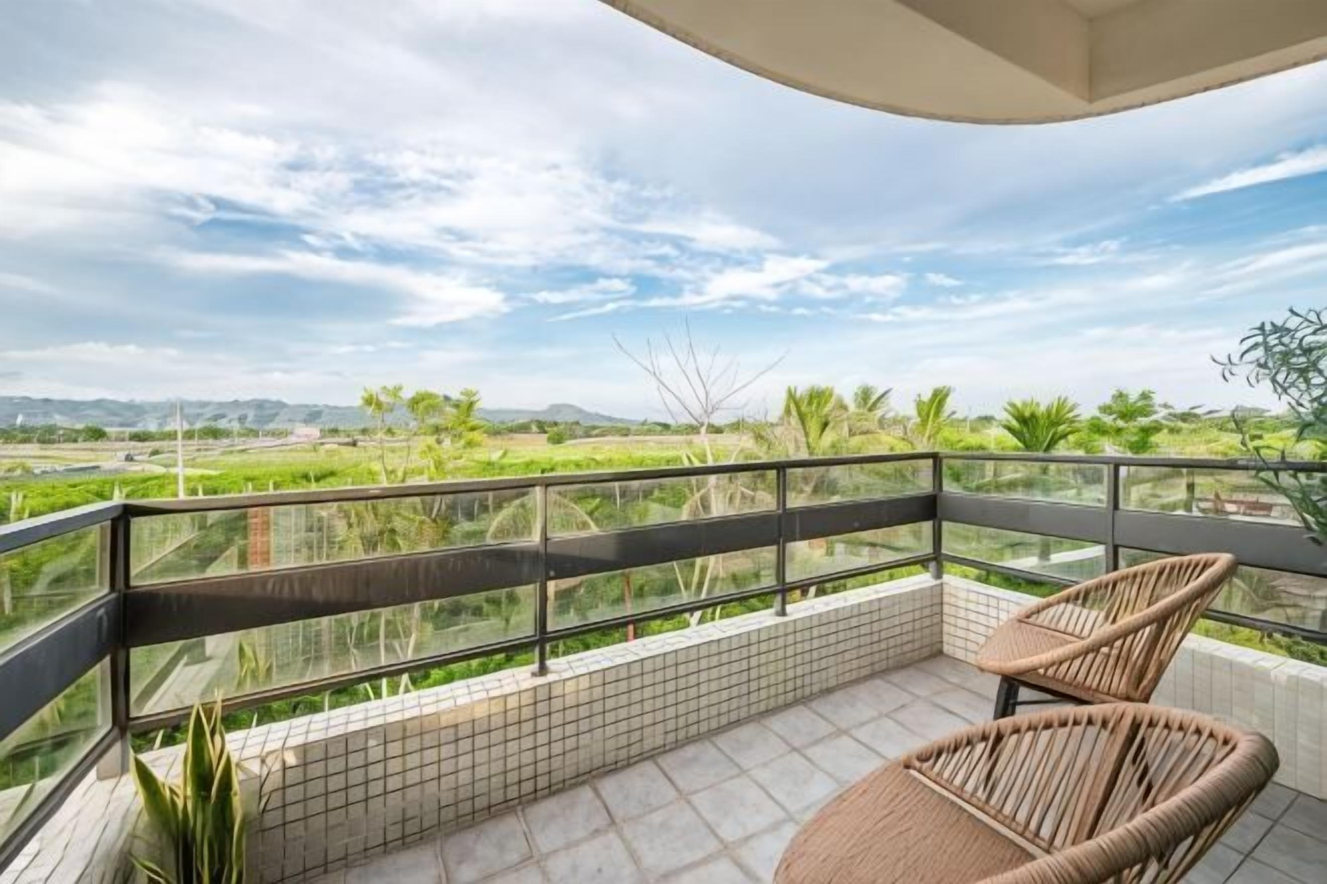 A balcony with a view of green fields and a clear sky.