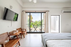 A bedroom with a bed, a TV, a desk with chairs, and a balcony with a table and chairs. - Rainbow Mansion (Taitung)