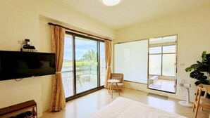 A bedroom with a large bed, a TV mounted on the wall, a sliding glass door to a balcony, and a small table with a chair. - Rainbow Mansion (Taitung)