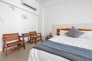 A hotel room with a bed, a desk, two chairs, a nightstand, and a wall-mounted air conditioner. - Rainbow Mansion (Taitung)