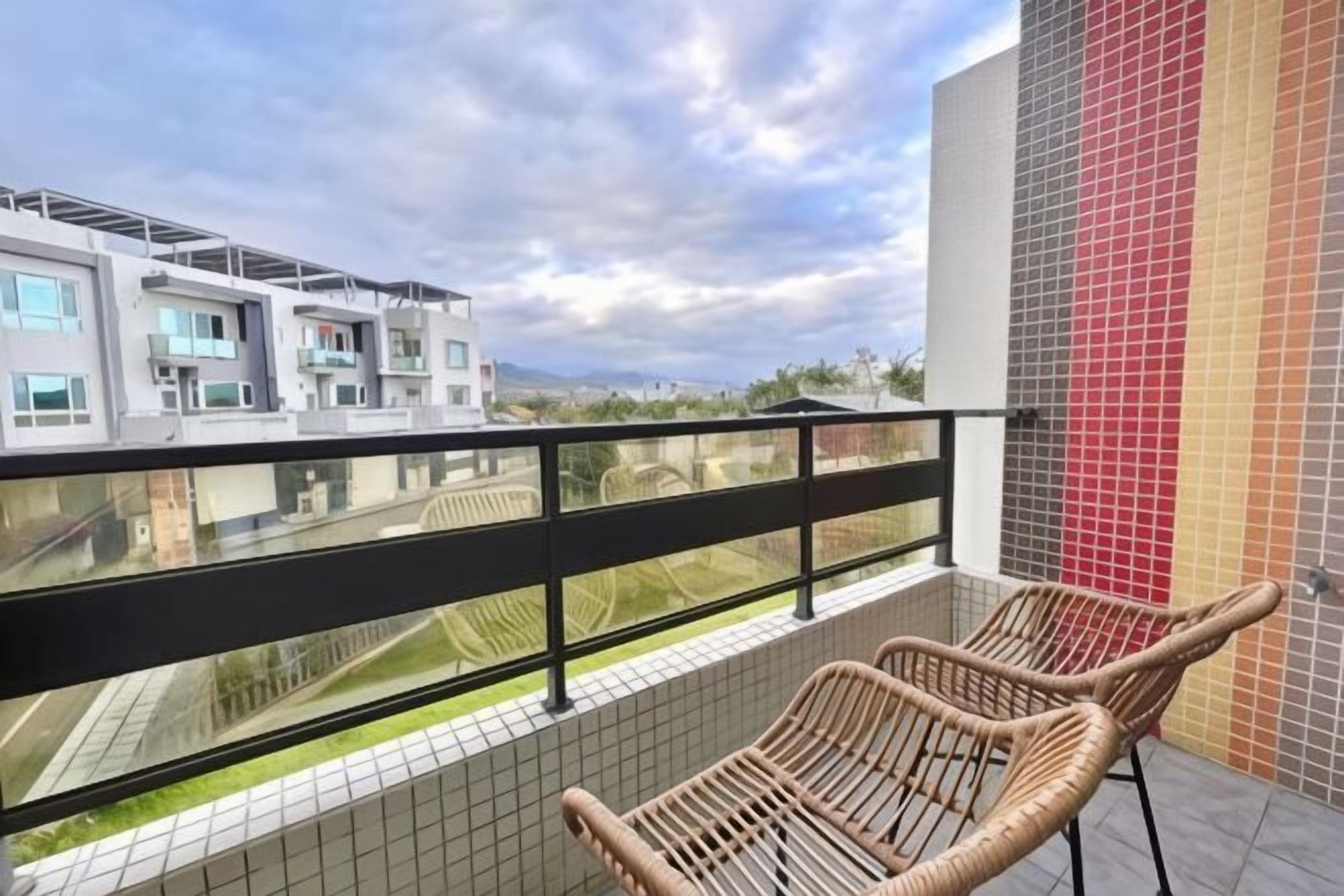 A balcony with wicker chairs, a glass railing, and a view of modern buildings.