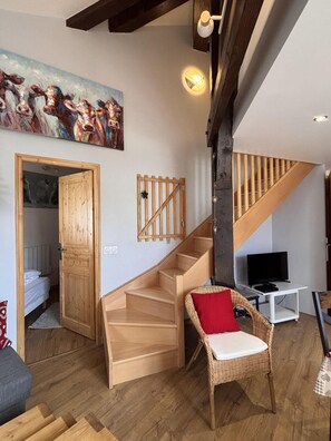 Ein geräumiger Raum mit einer Holztreppe, einem Fernseher, einem Korbstuhl und einem Gemälde an der Wand.