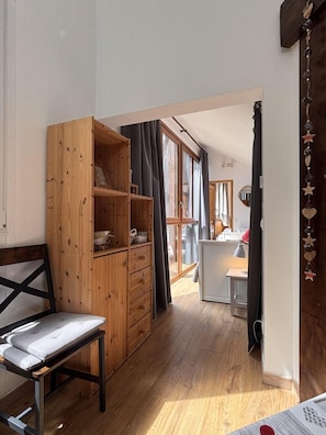Ein Zimmer mit einem Holzkabinett, einem Sessel und Blick in ein weiteres Zimmer mit Schreibtisch und Fenster.