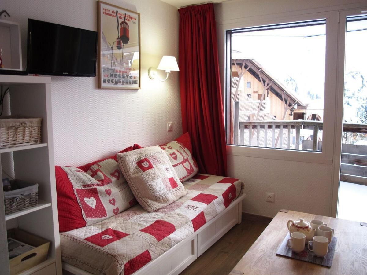 Una habitación acogedora con un sofá cama, una mesa de madera con tazas y un hervidor, un televisor, una lámpara y una ventana que ofrece vistas a un edificio.