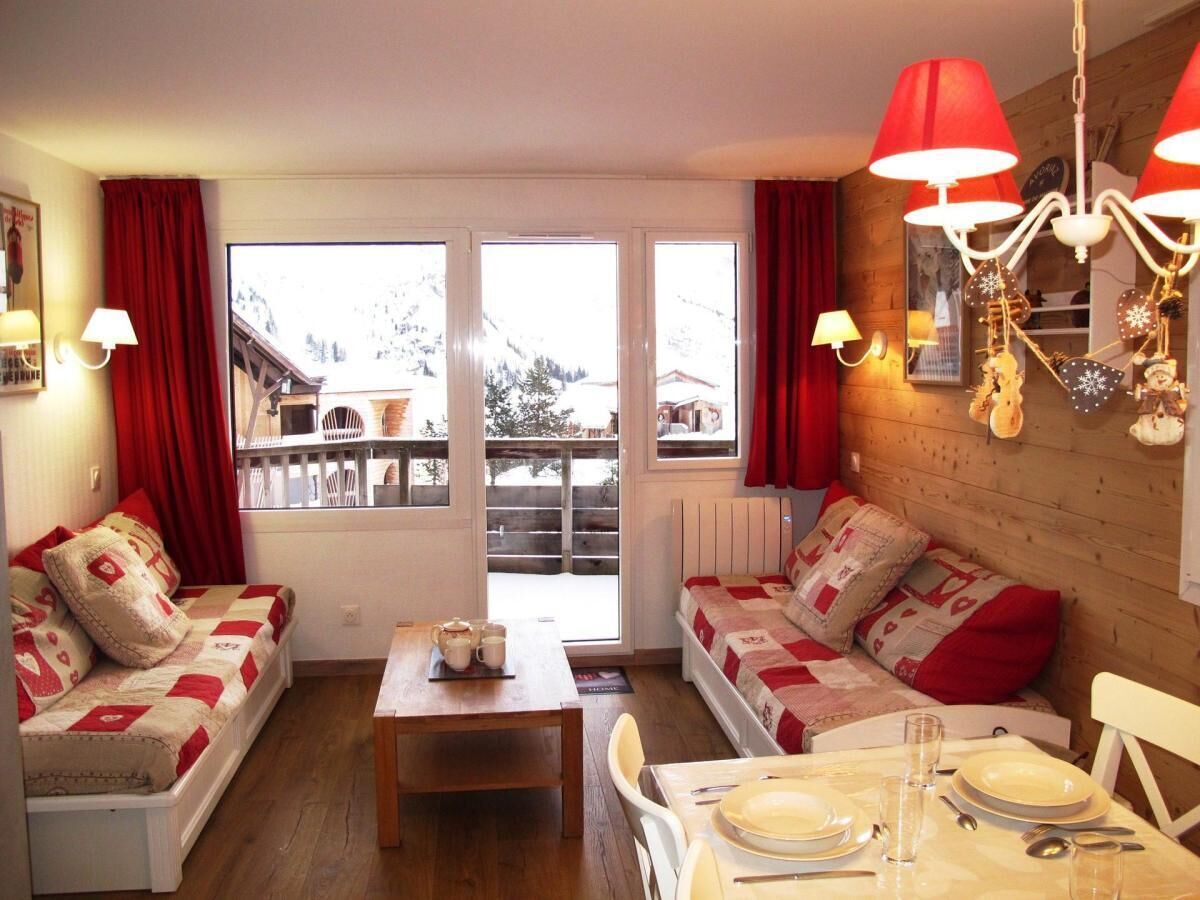 Una sala de estar acogedora con dos sofás, una mesa de comedor preparada para dos personas y un gran ventanal con vistas a una montaña nevada.