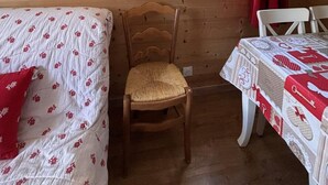 Puinen huone, jossa on sänky, tuoli, pöytä, koriste-esineillä täytetty hylly ja ikkuna, jossa on punainen verho.