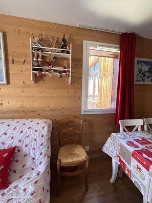 A wooden room with a bed, a chair, a table, a shelf with decorations, and a window with a red curtain. - 50m from resort center, 3rd floor, view mountain, balcony, tv, ski locker, 43m², Avoriaz (Avoriaz)
