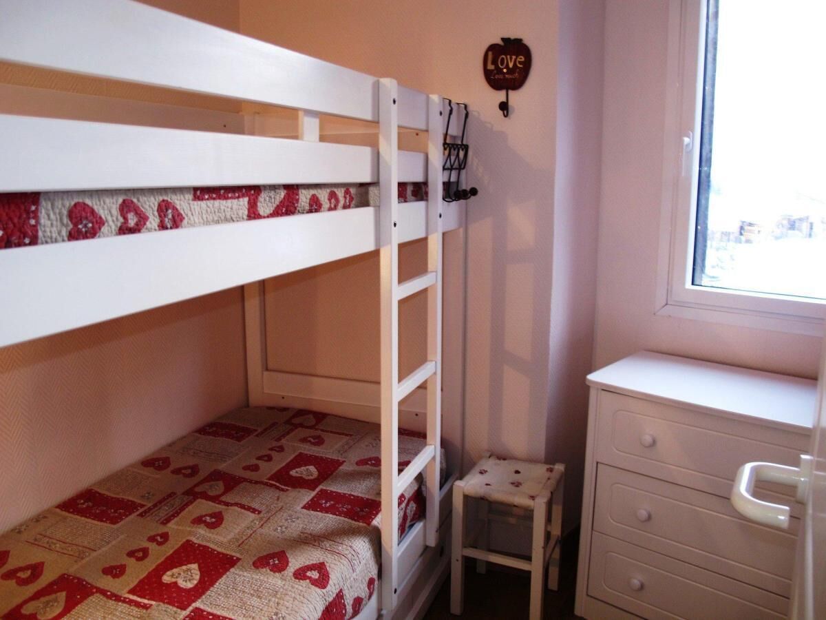 Ein Etagenbett mit gemustertem Bettbezug, ein kleiner Hocker, eine Kommode und ein Fenster mit Blick.