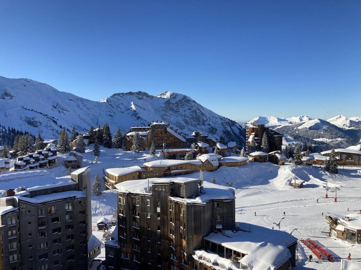 A snow-covered mountain resort with multiple buildings, ski slopes, and a clear blue sky.
