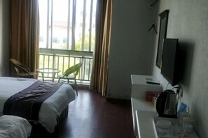 Habitación de hotel con cama, televisor, escritorio con cafetera y balcón con sillas.