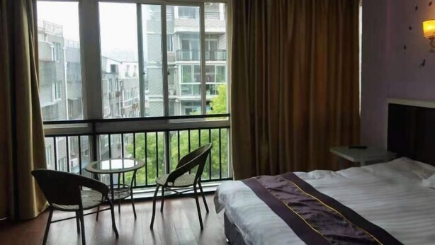 A hotel room with a balcony, a bed, a small table, and two chairs. - Xianju Tianyuan Hotel (Xianju)