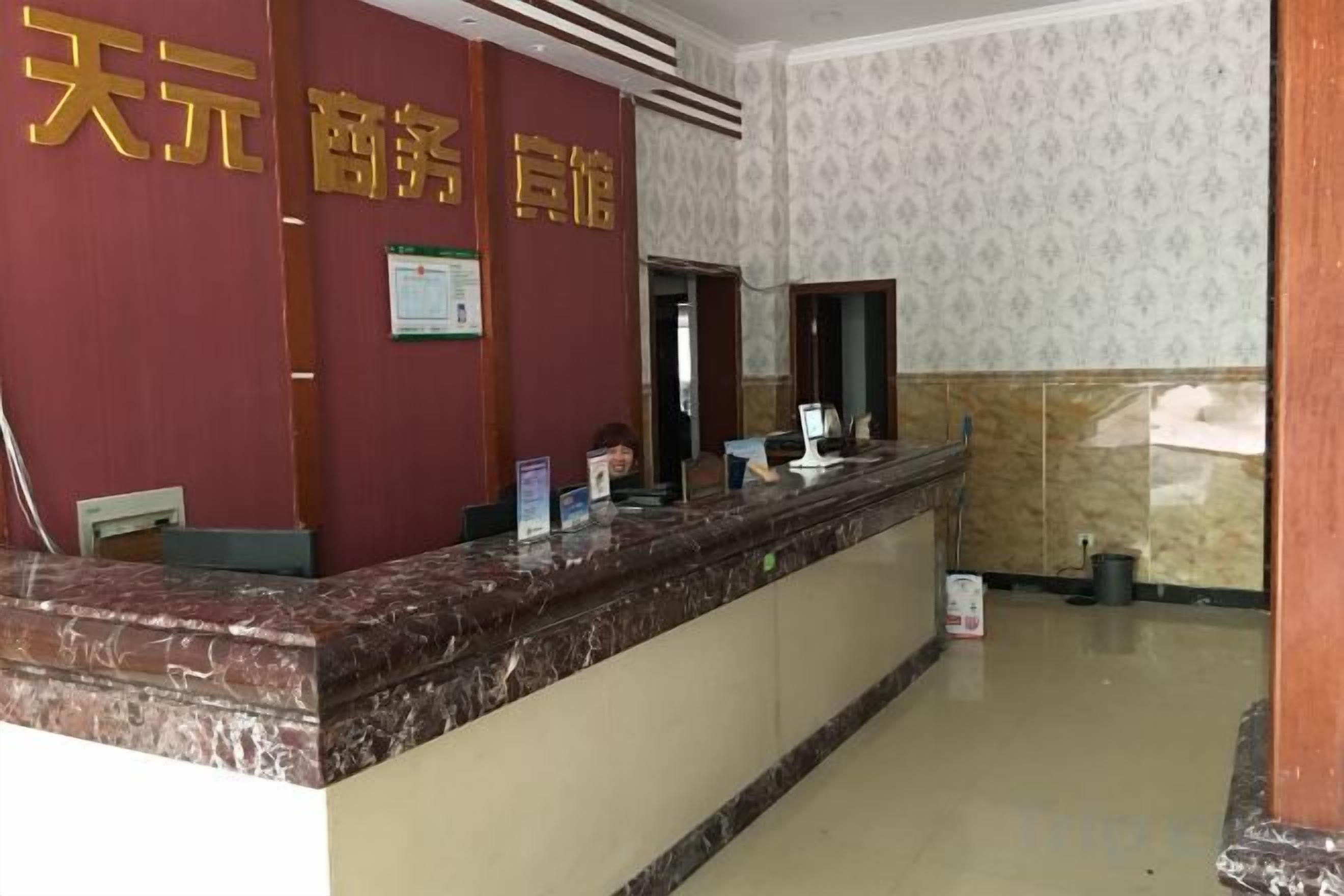 A hotel reception desk with a marble counter, a red wall with gold lettering, and a patterned wallpaper background.