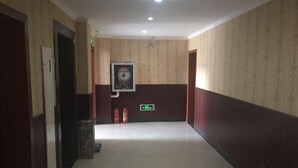 A hallway with patterned walls, a fire extinguisher, and an emergency exit sign. - Xianju Tianyuan Hotel (Xianju)