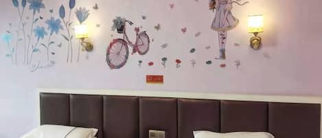 A hotel room with a bed, two bedside tables, and a wall with decorative wall art including flowers, a bicycle, and a girl.