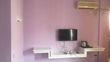 Una habitación con una televisión de pantalla plana montada en la pared, un estante blanco debajo y un equipo de aire acondicionado en la pared.