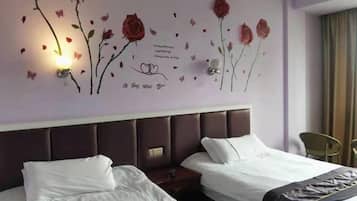 Habitación de hotel con dos camas, cabecera, decoración floral en la pared y una mesita de noche.
